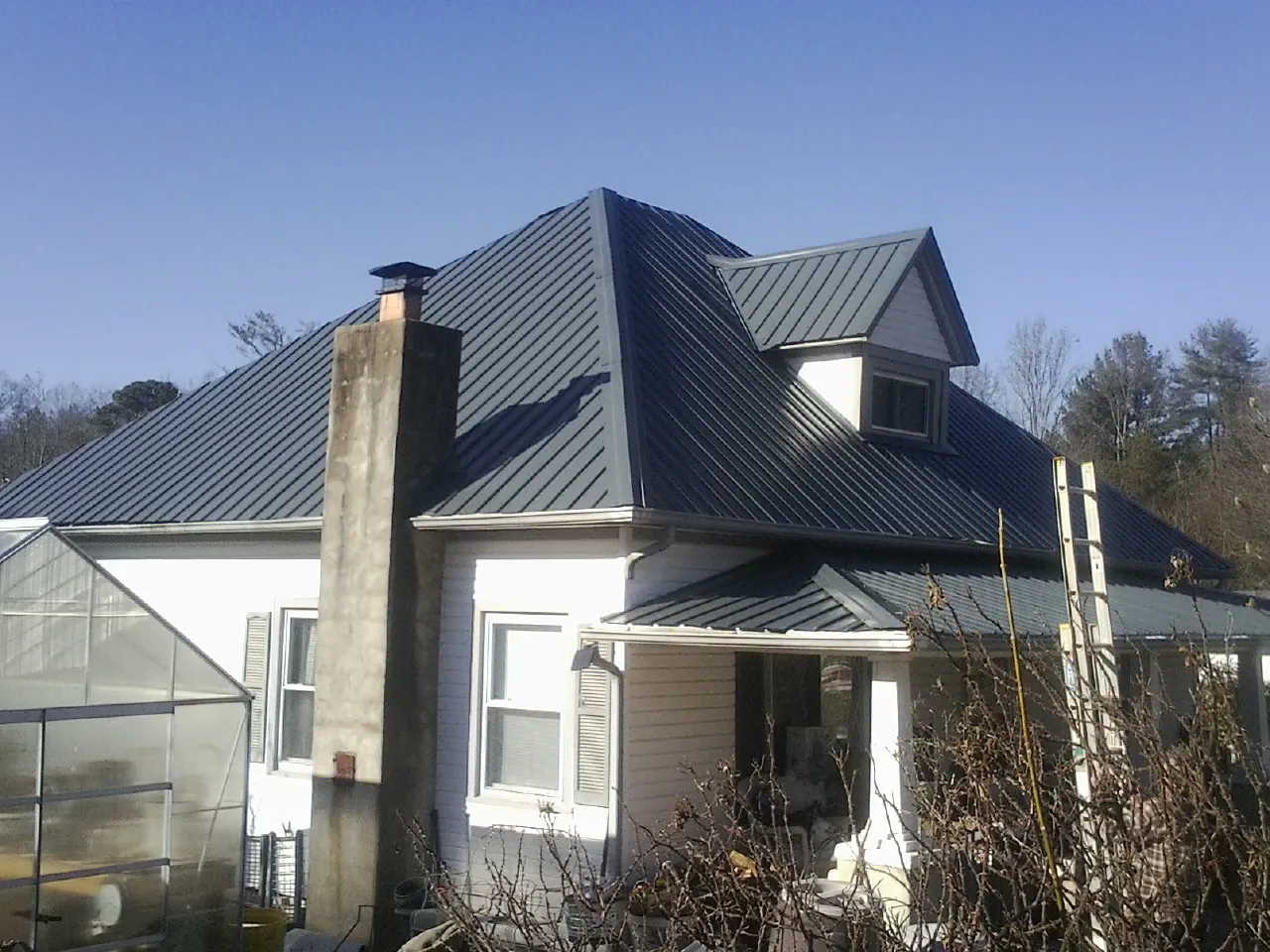 Dark blue standing seam metal roof on a white farmhouse with dormer — Slate & Tile Roof Repair by Roofing Brothers in West Hyannisport