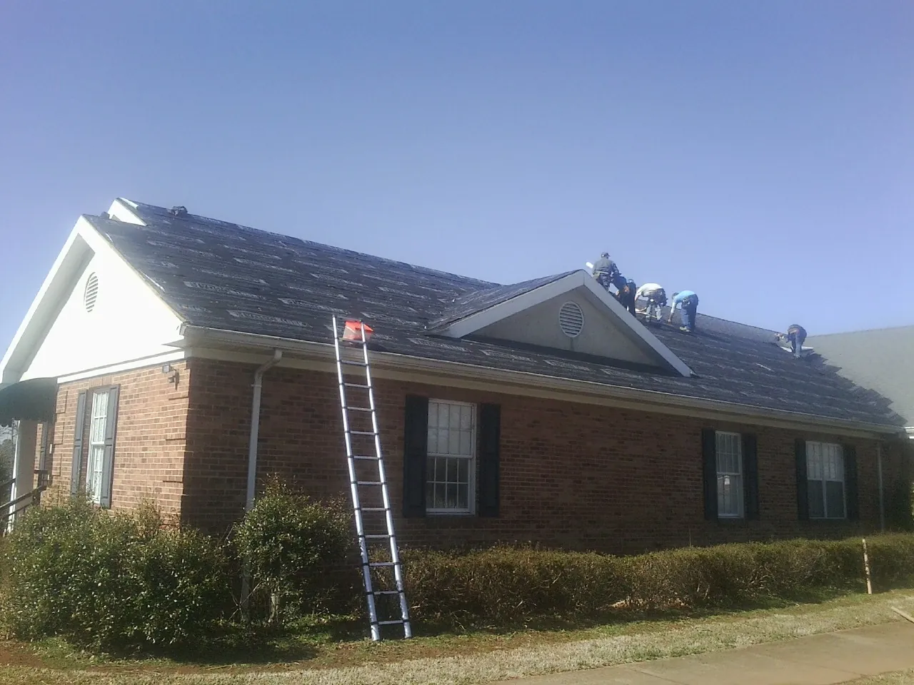 Crew tearing shingles off a brick ranch roof with a ladder set — Emergency Roof Repair work by our crew in West Hyannisport