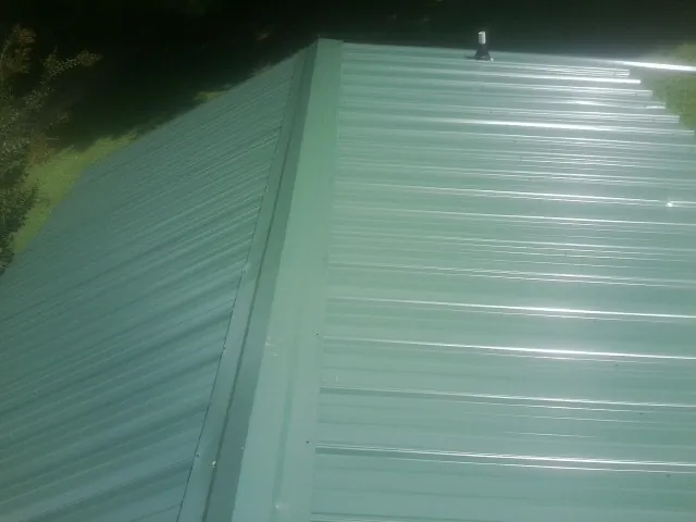 New green metal panels meeting at the ridge of a roof — Flat Roof Repair work by our crew in West Hyannisport