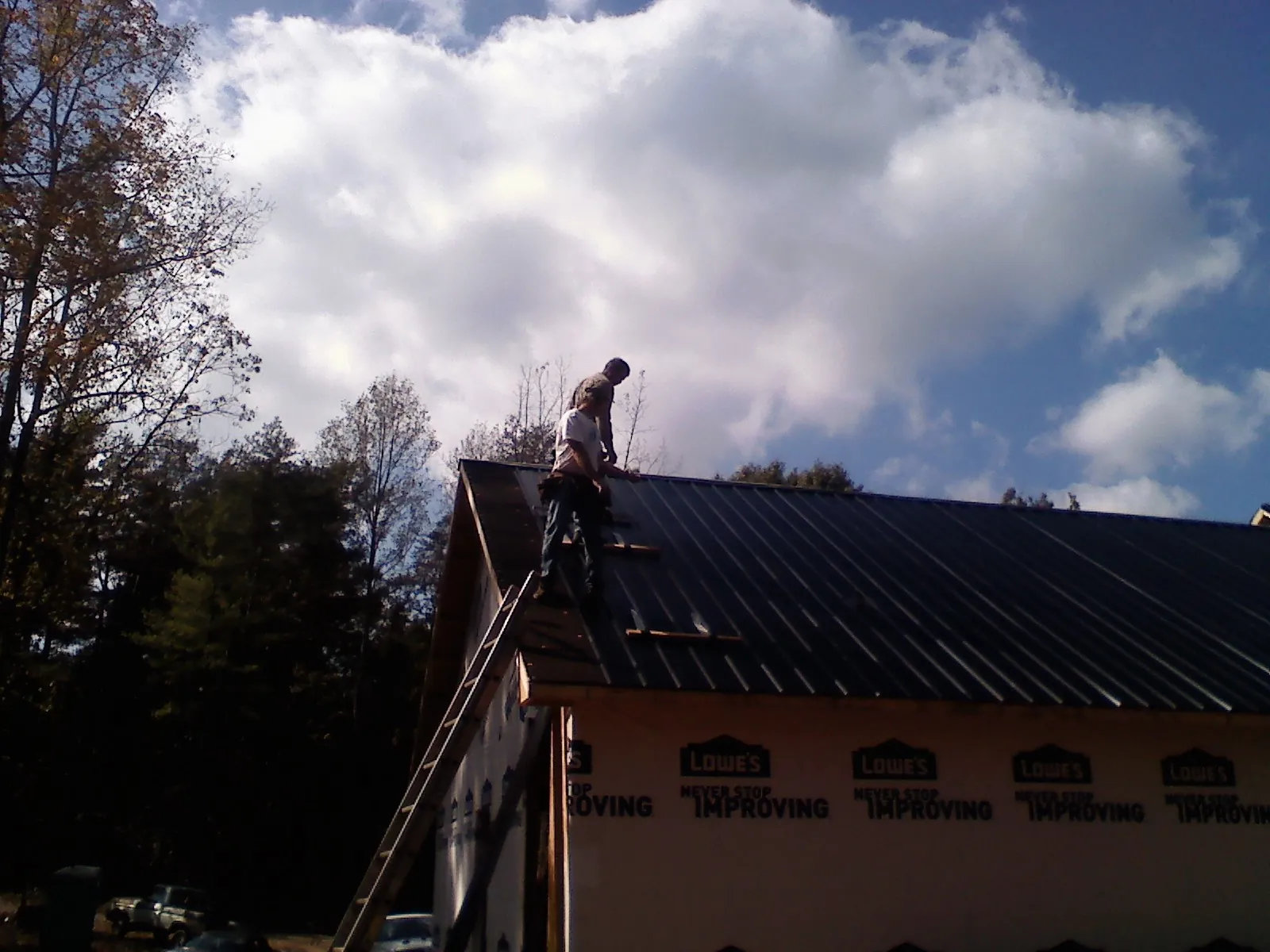 Roofer fastening dark metal panels high against a cloudy sky, from a Roof Inspection job in West Hyannisport