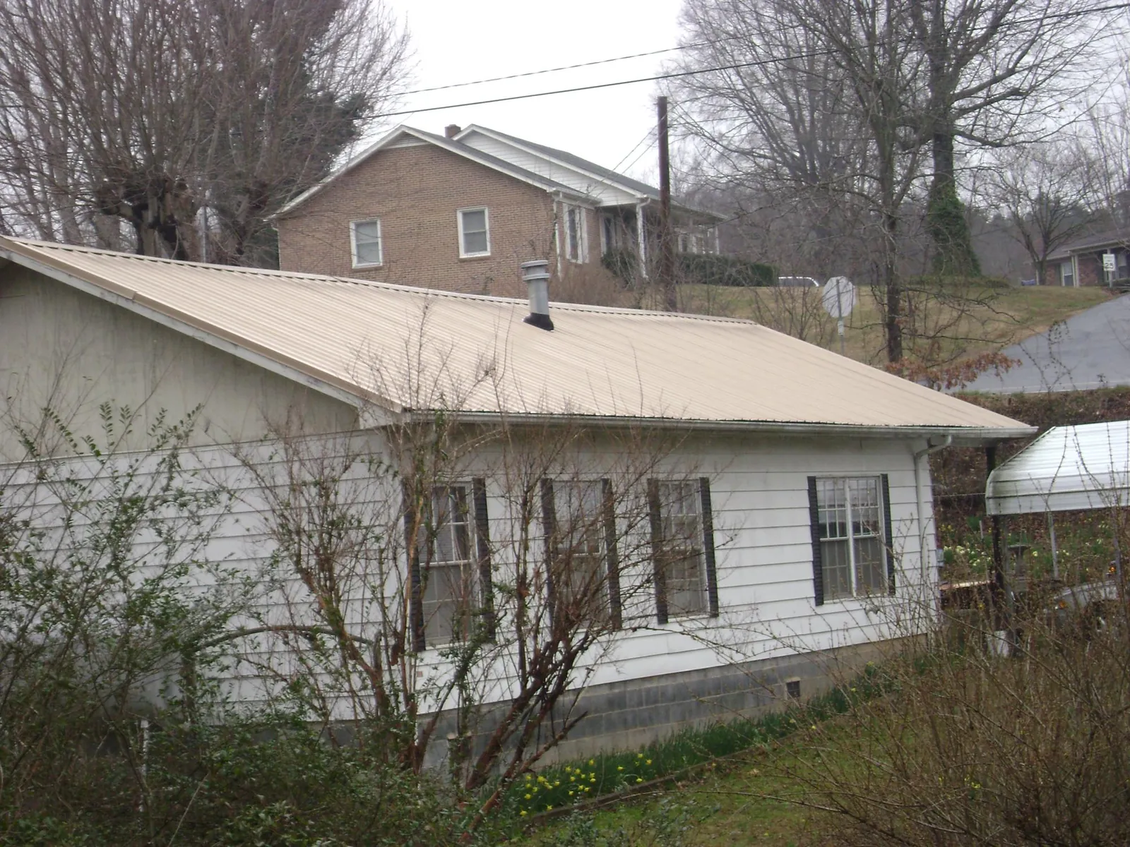 Tan metal roof on a white sided house set into a hillside — Commercial Roofing by Roofing Brothers in West Hyannisport